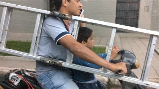 Un hombre hoy, en pleno centro de la ciudad, haciendo equilibrio entre un niño, una escalera y el celular.